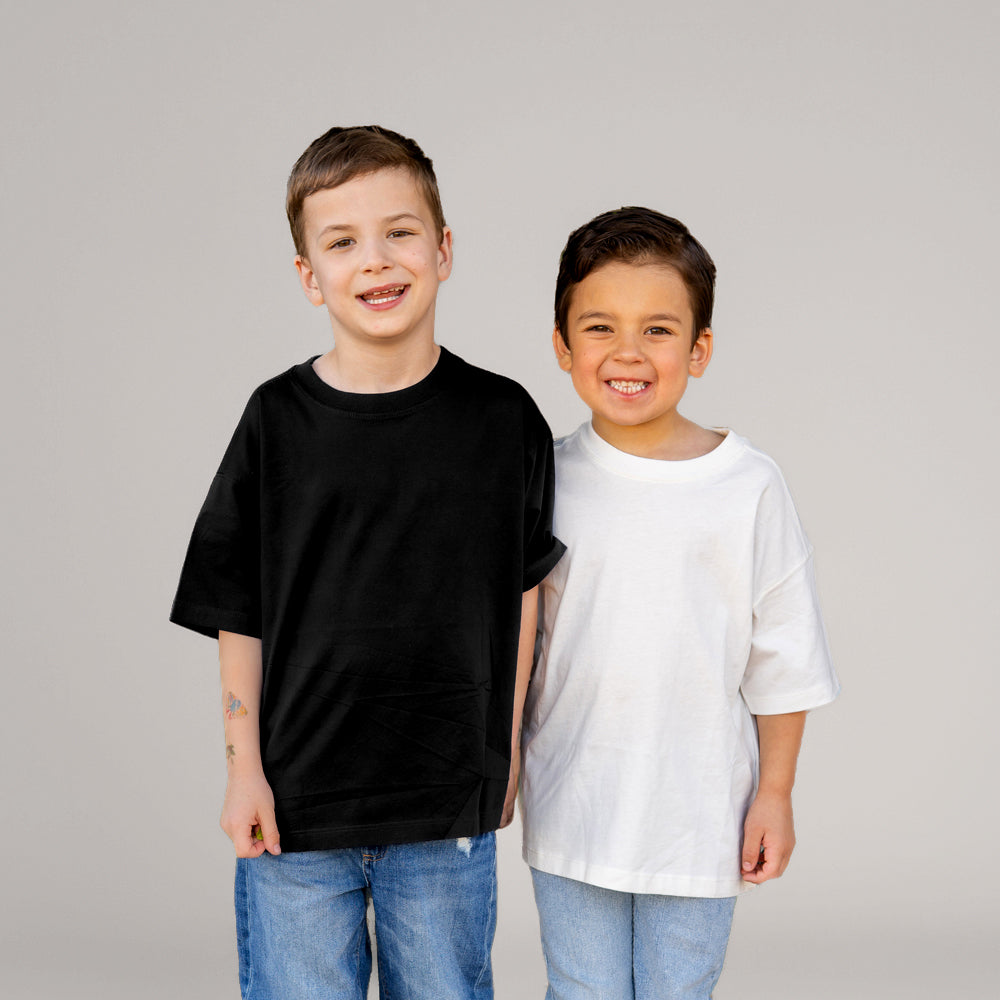 Two young boys standing side by side against a light gray studio background. The boy on the left wears a plain black short-sleeve T-shirt and blue jeans, while the boy on the right wears a plain white short-sleeve T-shirt and light blue jeans.