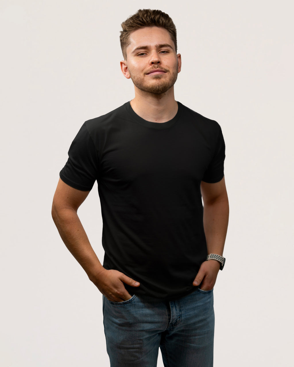 A man wearing a plain black short-sleeve crewneck t-shirt and blue jeans, standing against a light gray studio background.