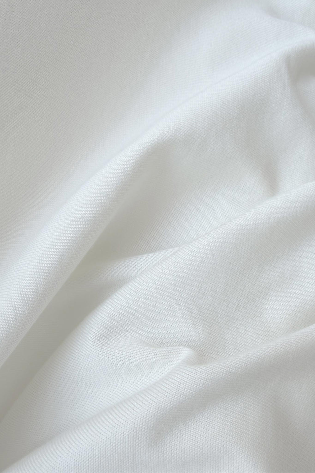 A close-up of draped white fabric with soft folds and a fine woven texture.