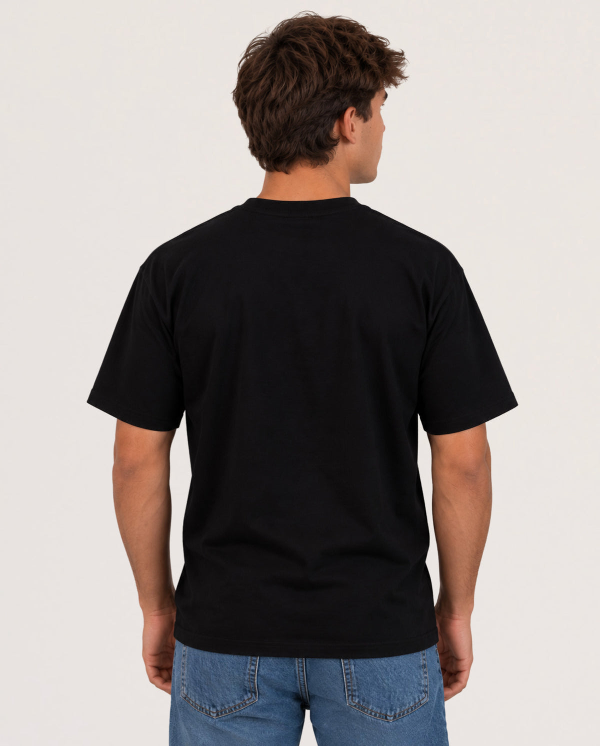 A man viewed from the back wearing a plain black short-sleeve crewneck t-shirt and blue jeans, standing against a light gray studio background.