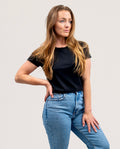 A woman modeling a black short-sleeve crewneck t-shirt paired with light wash blue jeans, posing against a solid light gray background.