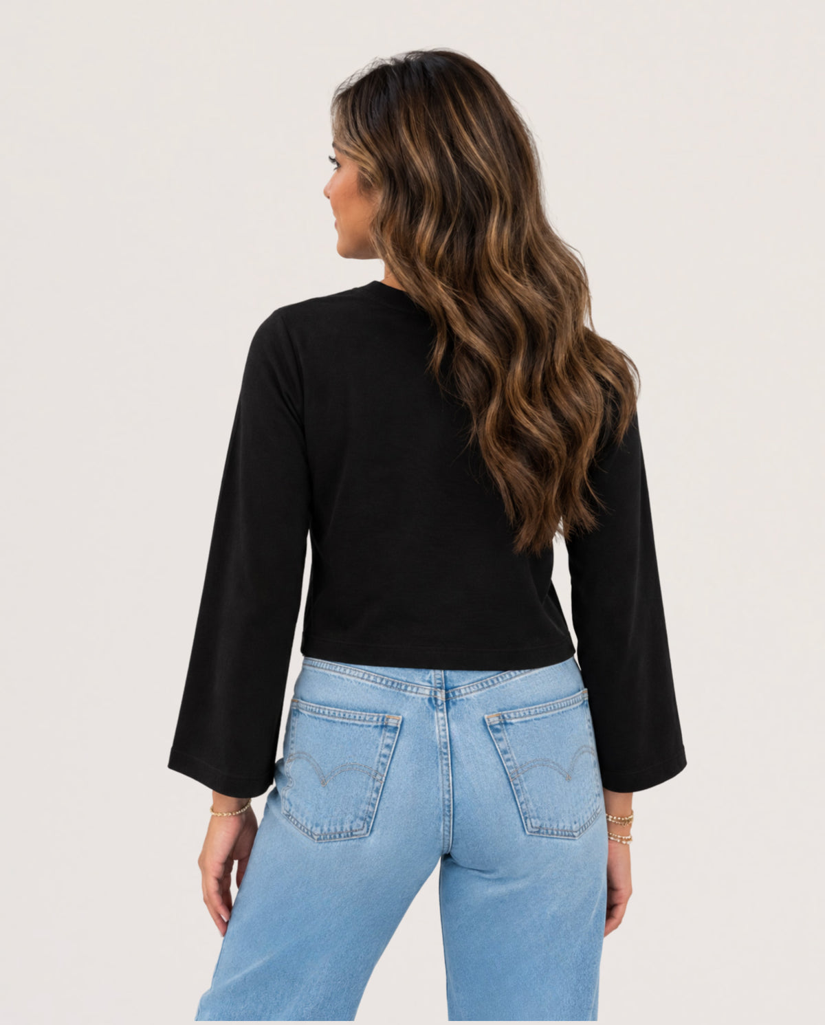 A woman shown from the back wearing a black long-sleeve crop top and light blue jeans against a plain light background.