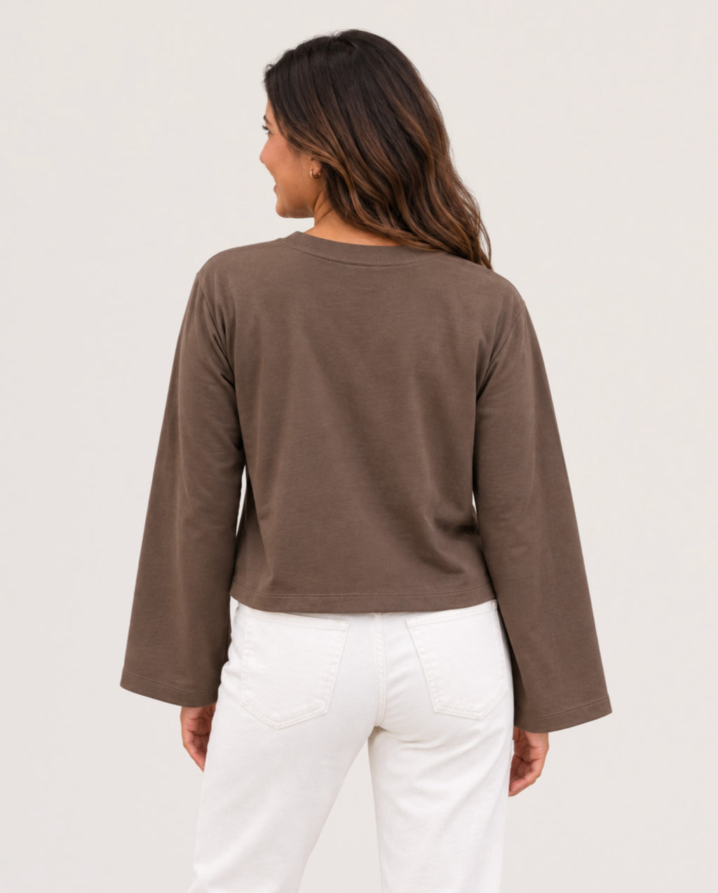 A woman shown from the back wearing a cropped, long-sleeve brown top and white pants against a plain light background.