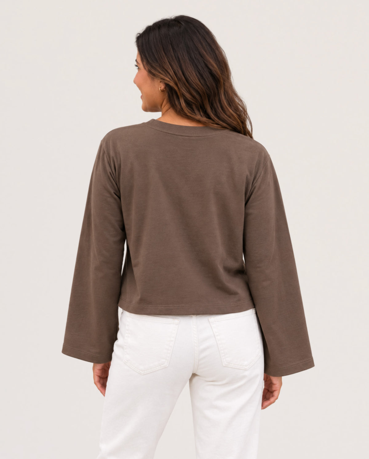 A woman shown from the back wearing a cropped, long-sleeve brown top and white pants against a plain light background.