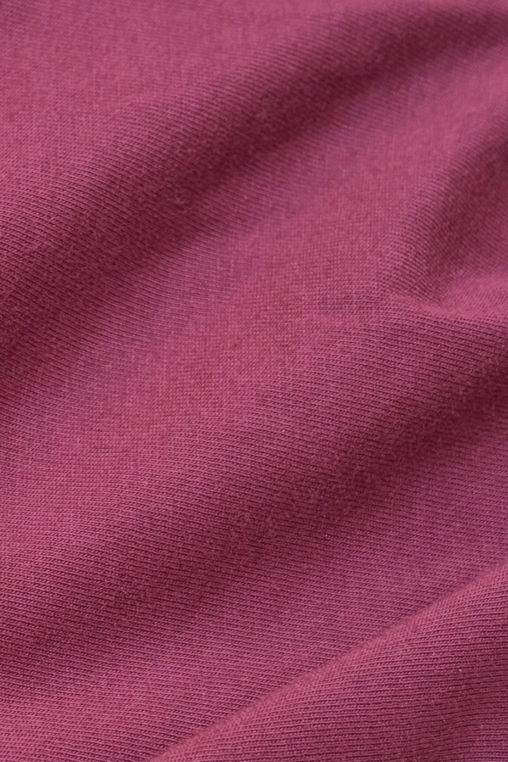 A close-up of draped fabric in a dusty rose or mauve pink color, showing the fine knit texture and soft folds.