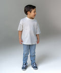 Child wearing a white t-shirt, blue jeans, and sneakers on a plain background
