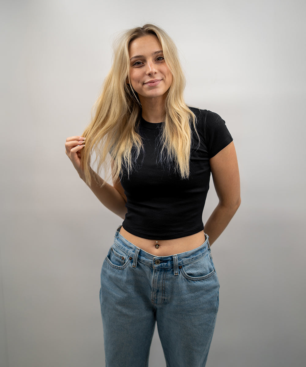 Woman wearing a black t-shirt and blue jeans against a plain background