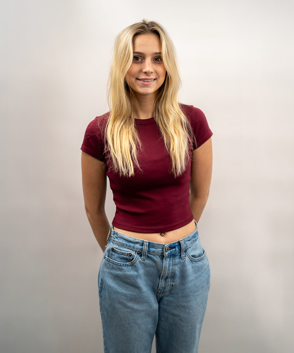 Woman wearing a maroon top and blue jeans against a plain background