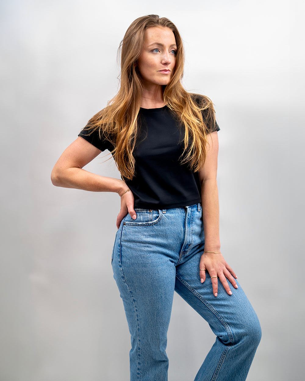 Woman wearing a black t-shirt and blue jeans against a plain background