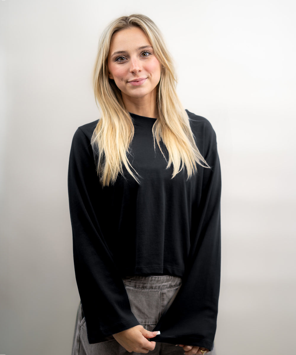 Person wearing a black long-sleeve top against a plain background