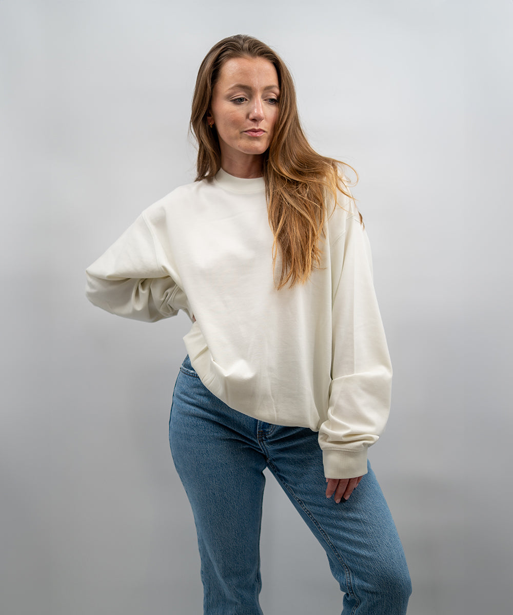 Woman wearing a white sweatshirt and blue jeans against a plain background