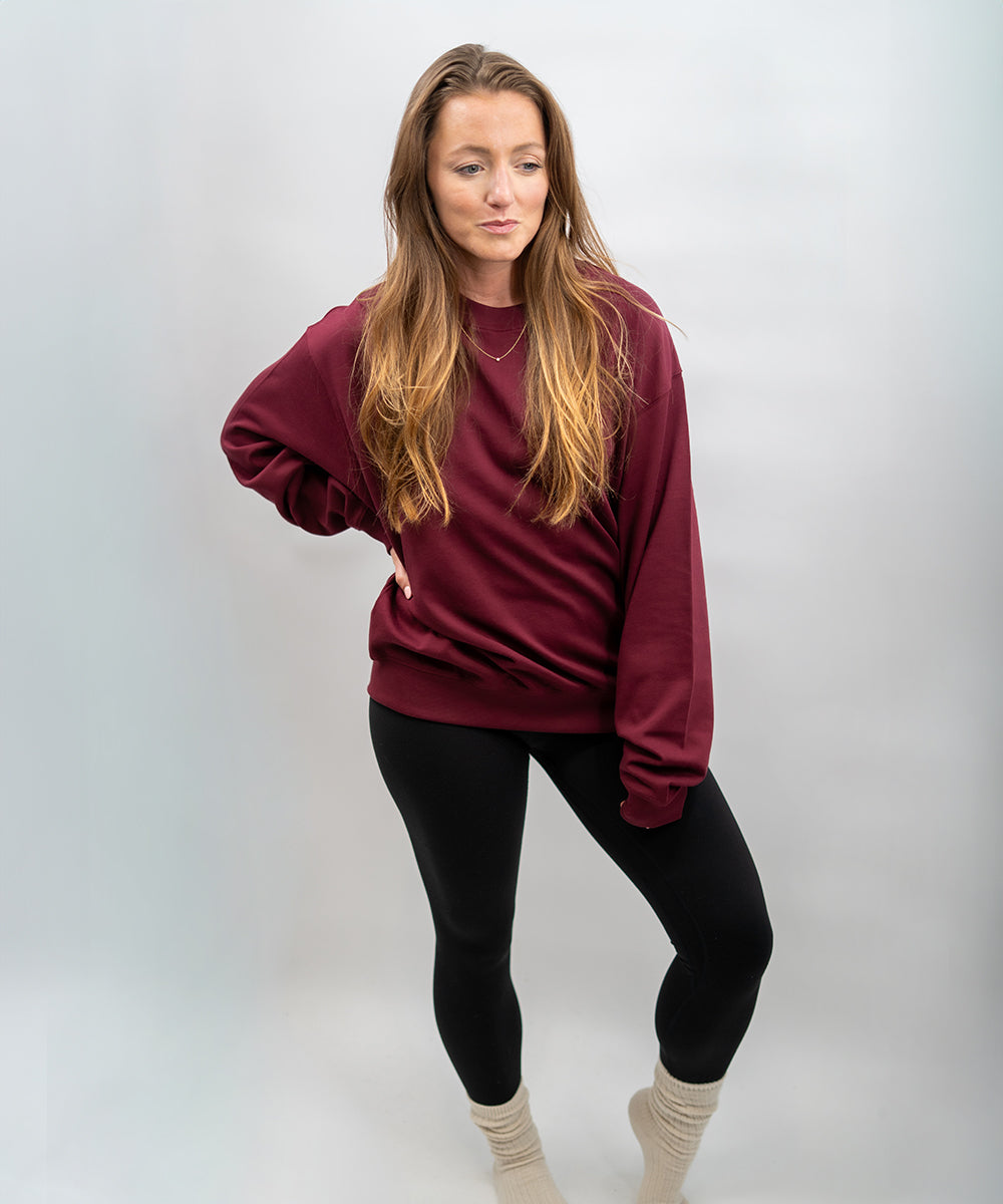 Woman wearing a maroon sweatshirt and black leggings against a white background